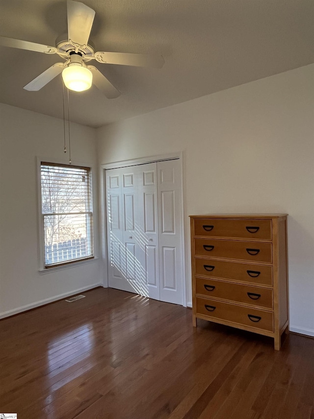 unfurnished bedroom with ceiling fan, dark wood-type flooring, and a closet