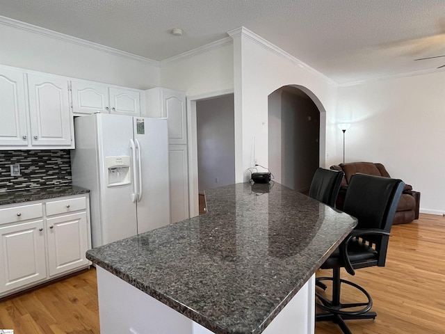 kitchen featuring a center island, white refrigerator with ice dispenser, backsplash, a breakfast bar, and white cabinets