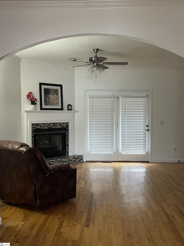 living room with ceiling fan, ornamental molding, a textured ceiling, a fireplace, and hardwood / wood-style flooring