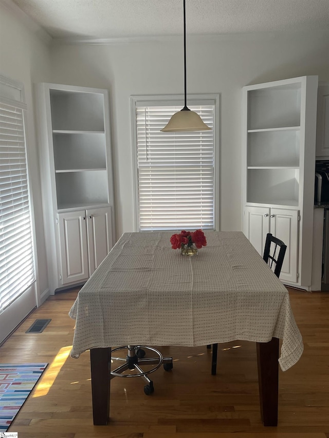 dining room with built in shelves, light hardwood / wood-style flooring, and a textured ceiling