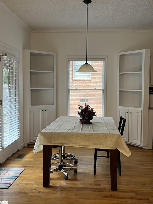 dining space featuring light wood-type flooring, a textured ceiling, a wealth of natural light, and crown molding