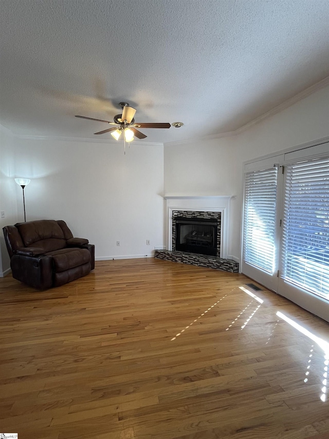 unfurnished living room featuring hardwood / wood-style floors, ceiling fan, a textured ceiling, and a tiled fireplace