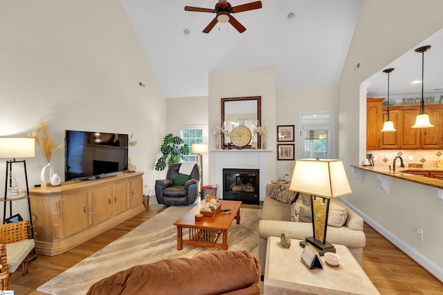 living room with light wood-type flooring, high vaulted ceiling, ceiling fan, and sink