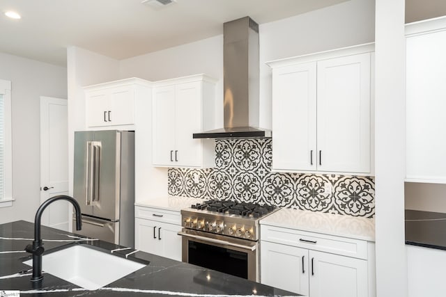 kitchen featuring premium appliances, white cabinetry, wall chimney exhaust hood, and sink