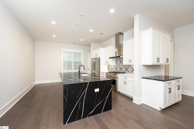 kitchen with high quality appliances, wall chimney range hood, sink, an island with sink, and dark hardwood / wood-style flooring