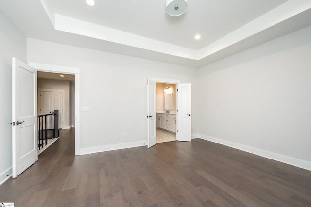 unfurnished bedroom with a tray ceiling, ensuite bath, and dark hardwood / wood-style floors