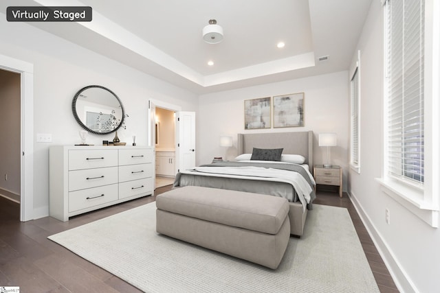 bedroom featuring connected bathroom, a tray ceiling, and dark wood-type flooring