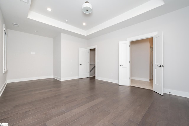 unfurnished bedroom with a raised ceiling and dark hardwood / wood-style flooring