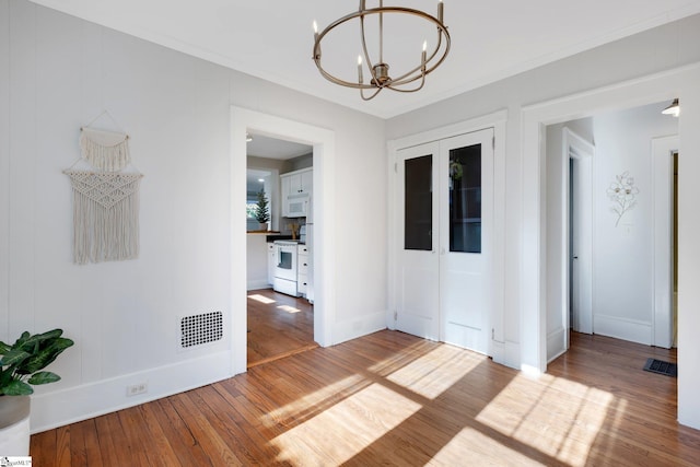 unfurnished room with crown molding, a notable chandelier, and hardwood / wood-style flooring