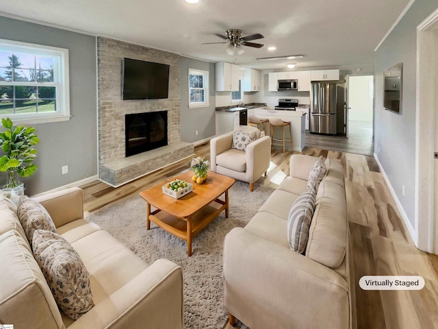 living room featuring ceiling fan, light hardwood / wood-style floors, crown molding, and a brick fireplace