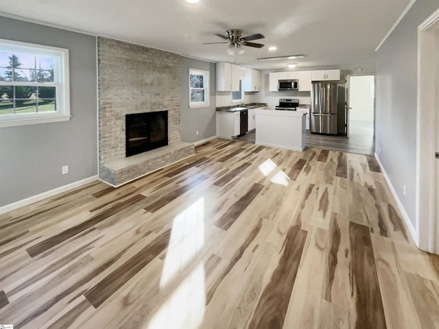 unfurnished living room with a brick fireplace, light hardwood / wood-style flooring, ceiling fan, and crown molding