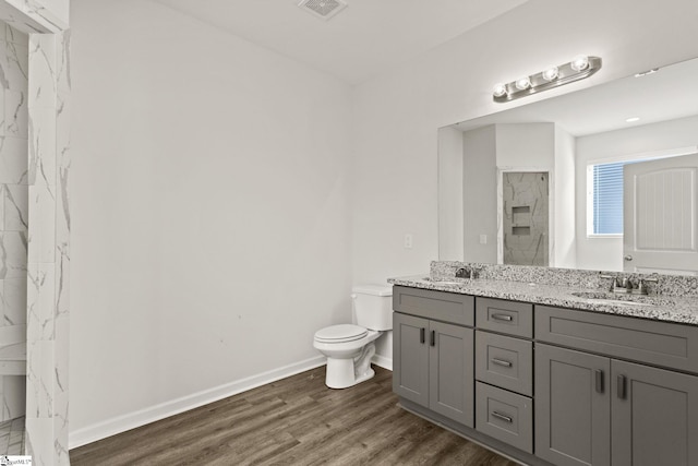 bathroom featuring hardwood / wood-style flooring, vanity, toilet, and a tile shower