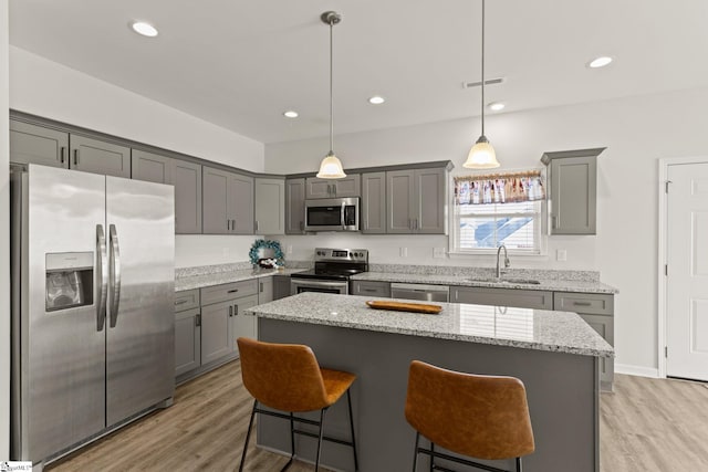 kitchen with sink, light hardwood / wood-style floors, decorative light fixtures, a kitchen island, and appliances with stainless steel finishes