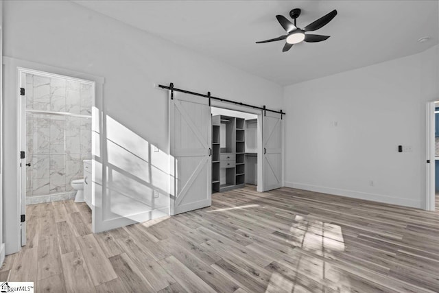 interior space with light wood-type flooring, a barn door, and ceiling fan