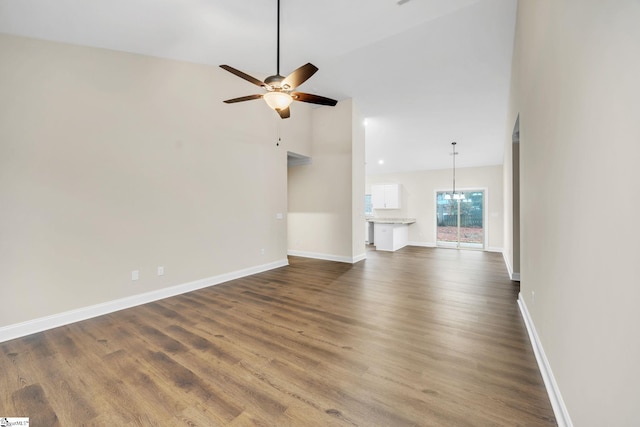 unfurnished living room with dark hardwood / wood-style flooring, high vaulted ceiling, and ceiling fan with notable chandelier