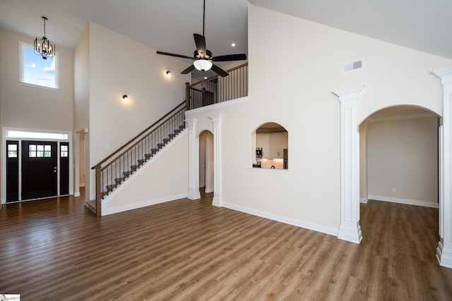 unfurnished living room featuring ceiling fan with notable chandelier, dark hardwood / wood-style floors, ornate columns, and a high ceiling