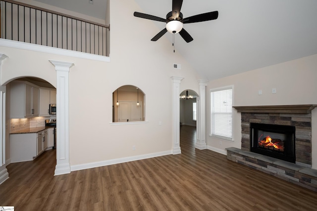 unfurnished living room with dark wood-type flooring, ceiling fan, high vaulted ceiling, decorative columns, and a fireplace