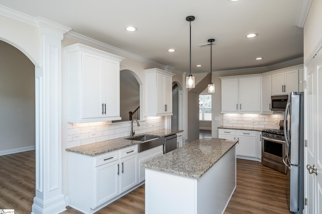 kitchen with sink, a kitchen island, stainless steel appliances, light stone countertops, and white cabinets