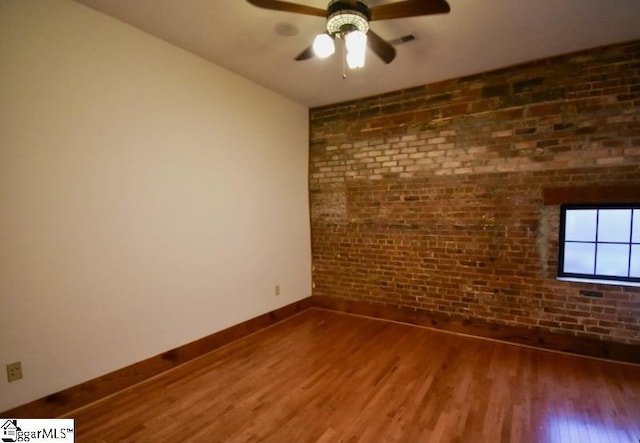 empty room with ceiling fan, wood-type flooring, and brick wall