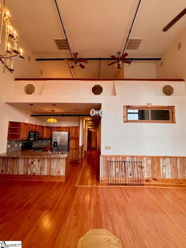 kitchen featuring stainless steel appliances, a high ceiling, kitchen peninsula, decorative backsplash, and light wood-type flooring