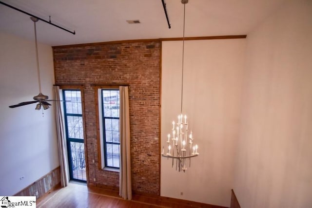 entryway featuring hardwood / wood-style floors, ceiling fan with notable chandelier, and brick wall