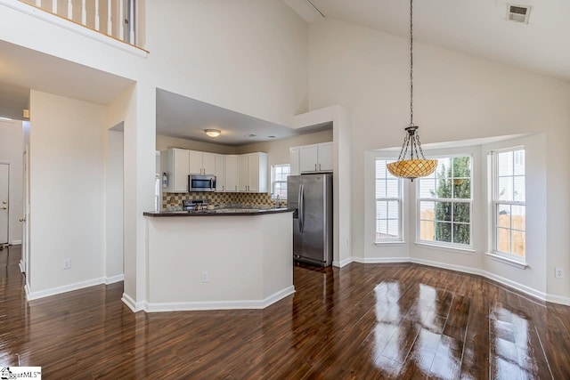 kitchen featuring white cabinets, appliances with stainless steel finishes, decorative light fixtures, and high vaulted ceiling