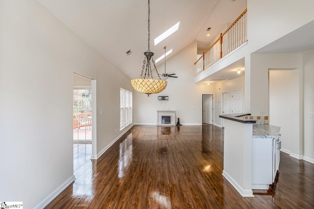 kitchen with dark wood-type flooring, high vaulted ceiling, hanging light fixtures, ceiling fan, and kitchen peninsula