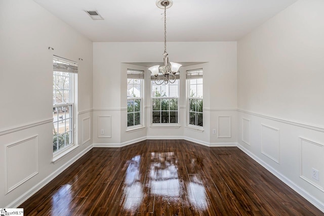 unfurnished dining area with dark wood-type flooring and an inviting chandelier