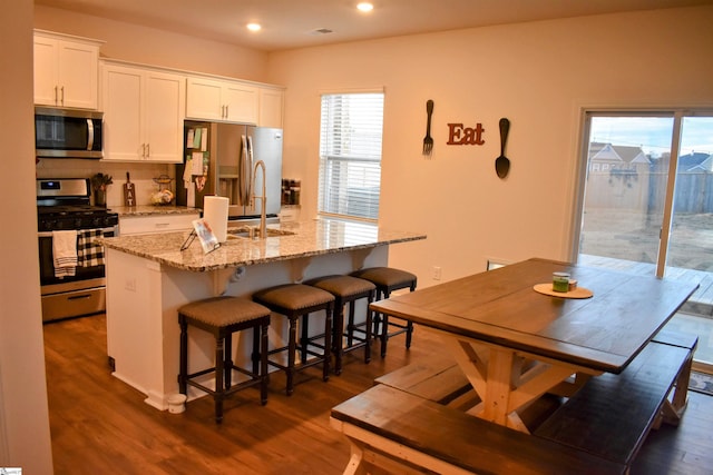 kitchen featuring dark wood-type flooring, a center island with sink, white cabinets, and stainless steel appliances