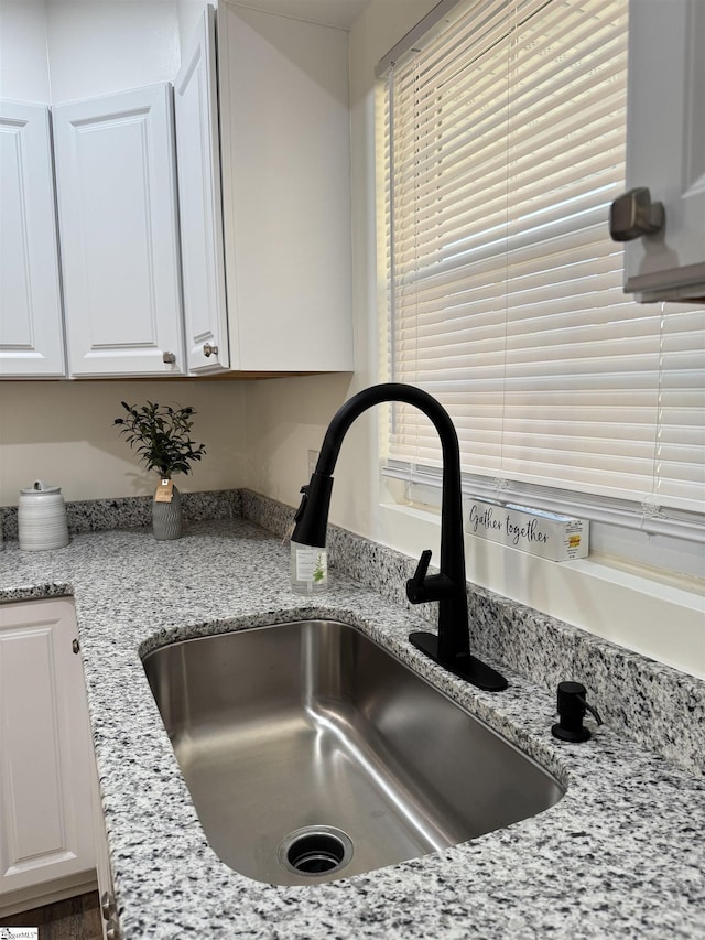 room details featuring sink, white cabinets, and light stone counters