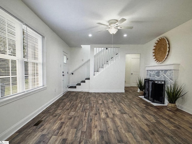 living room featuring a stone fireplace, dark hardwood / wood-style floors, and ceiling fan