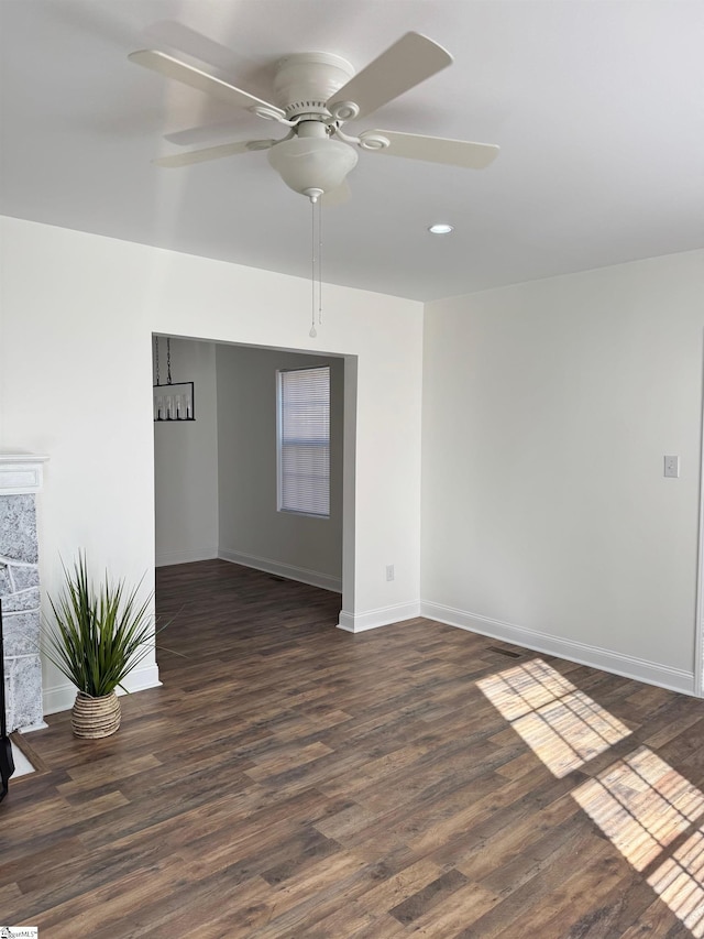 empty room featuring dark wood-type flooring, ceiling fan, and a stone fireplace