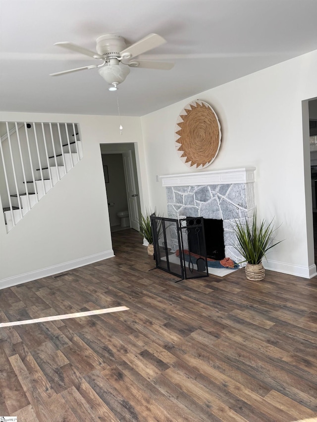 living room featuring dark hardwood / wood-style floors, ceiling fan, and a stone fireplace