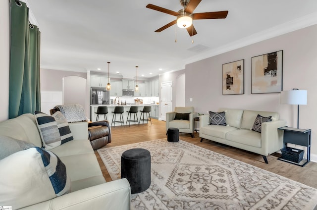 living room with crown molding, light hardwood / wood-style flooring, and ceiling fan