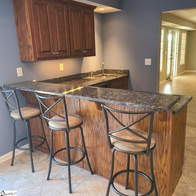 kitchen with a kitchen bar, kitchen peninsula, sink, and light tile patterned floors