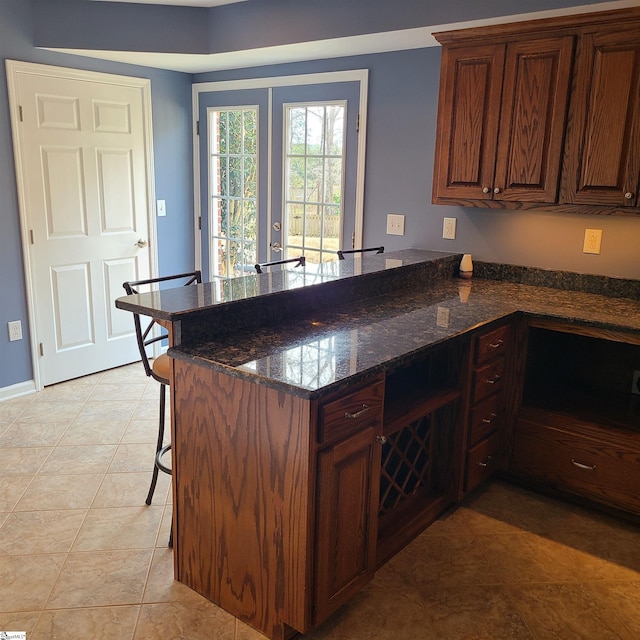 kitchen with a breakfast bar, dark stone counters, french doors, light tile patterned flooring, and kitchen peninsula