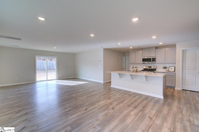 kitchen with gray cabinetry, a kitchen island with sink, light hardwood / wood-style floors, and appliances with stainless steel finishes