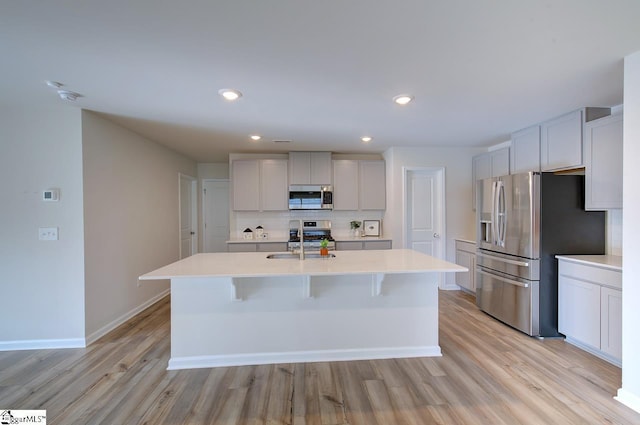 kitchen with decorative backsplash, appliances with stainless steel finishes, a kitchen island with sink, sink, and light hardwood / wood-style floors