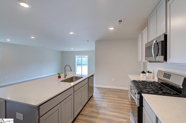 kitchen featuring sink, light hardwood / wood-style flooring, an island with sink, appliances with stainless steel finishes, and tasteful backsplash