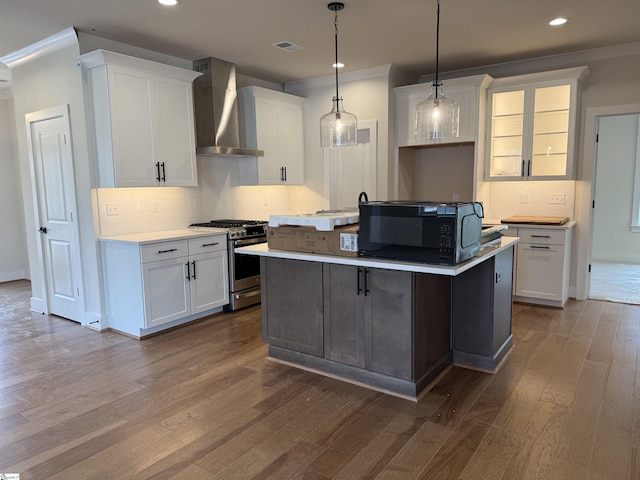 kitchen featuring white cabinets, wall chimney range hood, gas range, an island with sink, and wood-type flooring