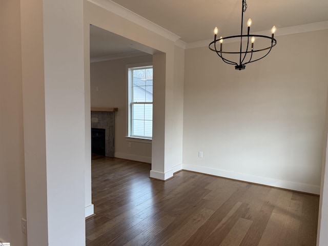 unfurnished dining area featuring crown molding, dark wood-type flooring, a tile fireplace, and an inviting chandelier