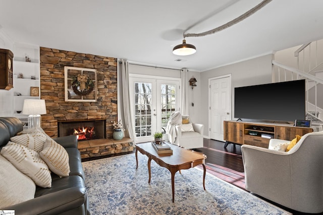 living room featuring a stone fireplace, french doors, ornamental molding, and hardwood / wood-style flooring