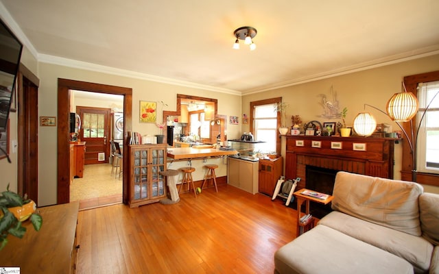 sitting room featuring a brick fireplace, ornamental molding, stacked washer and dryer, and light hardwood / wood-style flooring