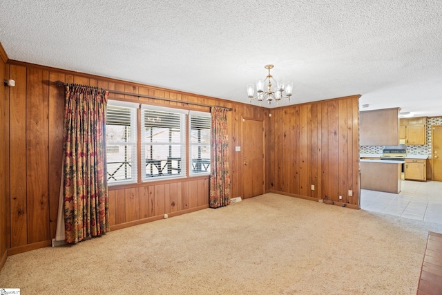 spare room featuring light carpet, an inviting chandelier, and wooden walls