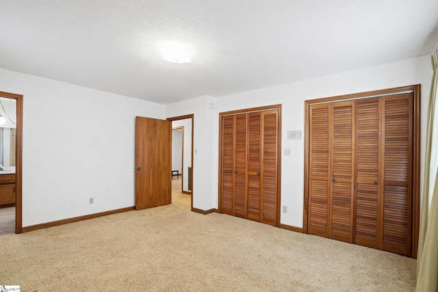 unfurnished bedroom featuring two closets, connected bathroom, a textured ceiling, and light colored carpet