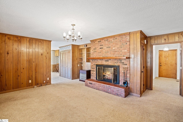 unfurnished living room with a brick fireplace, built in features, an inviting chandelier, and wooden walls