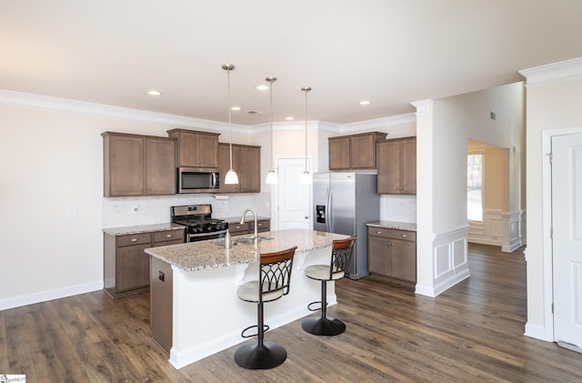 kitchen with pendant lighting, a center island with sink, sink, appliances with stainless steel finishes, and light stone counters