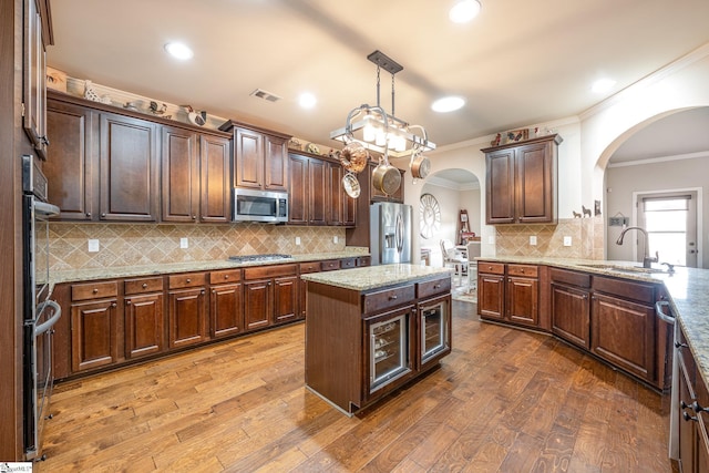 kitchen with pendant lighting, sink, hardwood / wood-style flooring, ornamental molding, and appliances with stainless steel finishes