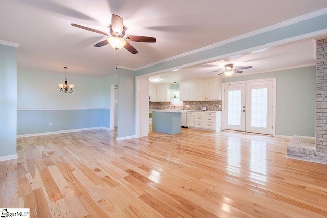 unfurnished living room with ceiling fan with notable chandelier, ornamental molding, french doors, and light hardwood / wood-style flooring