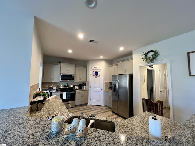 kitchen with appliances with stainless steel finishes, backsplash, sink, stone countertops, and light hardwood / wood-style flooring